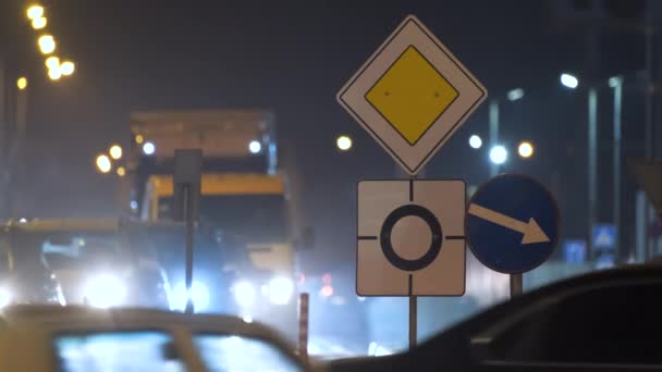 Roundabout οδικές πινακίδες με θολή αυτοκίνητα στην κυκλοφορία της πόλης το βράδυ. Έννοια των αστικών μεταφορών — Αρχείο Βίντεο