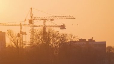 Gün batımında yüksek apartmanlı inşaat alanındaki vinçlerin koyu renkli silueti. Gayrimenkul geliştirme