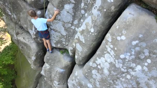 Entschlossener Jungenkletterer, der die steile Wand des felsigen Berges hochklettert. Kind überwindet schwierige Strecke. Extremsport und Kletterhobby-Konzept — Stockvideo