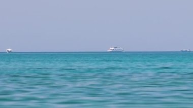 Mavi deniz suyunun dalgalı yüzeyi ve sakin dalgalar üzerinde yüzen uzak gemileri olan deniz burnu.