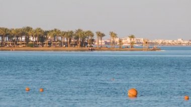 Deniz yüzeyinde yüzen sarı şamandıralar, kıyı şeridi manzaralı tropikal tatil beldesindeki derin sularda yüzme kısıtlamalarını işaret ediyor. İnsan hayatı güvenliği kavramı
