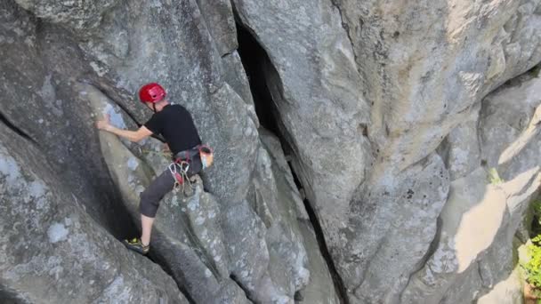 Joven escalando empinada pared de montaña rocosa. Hombre escalador supera ruta desafiante. Participar en el concepto de deporte extremo — Vídeo de stock