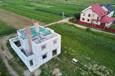 Havalandırılmış hafif beton duvarları ve inşaat halindeki ahşap çatı kirişleri olan bitmemiş özel evin havadan görüntüsü.