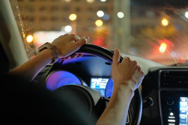 Sürücü ellerinin direksiyon tutarak kapanması ve arka planda şehir ışıklarının bulanıklaşması.