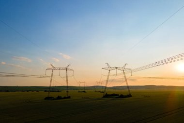Gün batımında elektrik hatları olan yüksek voltaj kuleleri.