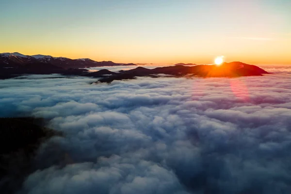 Vista aérea del vibrante amanecer sobre densas nubes blancas con lejanas montañas oscuras en el horizonte — Foto de Stock