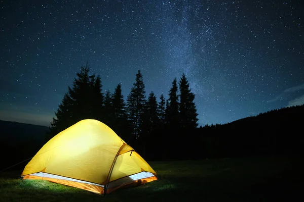 Tenda de acampamento brilhantemente iluminada brilhando no acampamento em montanhas escuras sob estrelas da noite céu coberto. Estilo de vida ativo e conceito de viagem — Fotografia de Stock