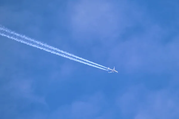 Avião de passageiros distantes voando em alta altitude através de nuvens brancas no céu azul deixando traços de fumaça branca de contrail para trás. Conceito de transporte aéreo — Fotografia de Stock