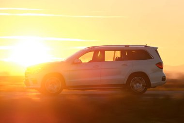 Gün batımında şehirlerarası yolda hızla giden bir SUV arabası. Akşamları otoyol trafiği