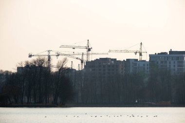 Göl kıyısında inşaat halindeki vinçler ve yüksek konutlu binalar. Gayrimenkul geliştirme