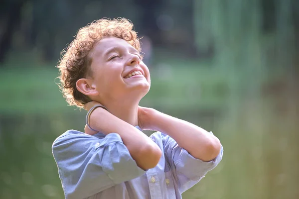 Młody, szczęśliwy chłopiec relaksujący się w letnim parku. Pozytywny dzieciak cieszący się latem na świeżym powietrzu. Koncepcja dobrostanu dzieci — Zdjęcie stockowe