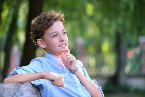 Молодий щасливий хлопчик розслабляється, сидячи на лавці в літньому парку. Позитивна дитина насолоджується літнім часом на відкритому повітрі. Концепція добробуту дітей — стокове фото
