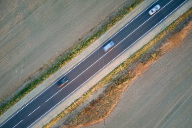 Gün batımında hızlı giden arabalarla şehirlerarası yol manzarası. Akşamları otoban trafiğinin insansız hava aracı görüntüsü