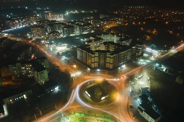 Widok z powietrza na wysokie budynki mieszkalne i jasne oświetlone skrzyżowanie ronda na ulicy miejskiej w dzielnicy mieszkalnej miasta w nocy. Ciemny krajobraz miejski — Zdjęcie stockowe