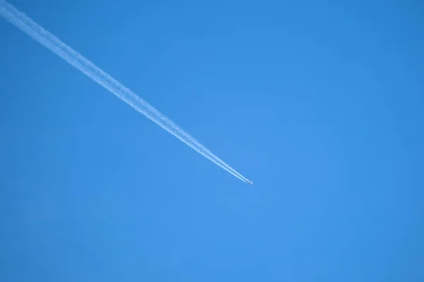 Vzdálené letadlo osobního tryskáče letí ve vysoké nadmořské výšce na jasně modré obloze a zanechává za sebou stopy bílého kouře. Koncept letecké dopravy — Stock fotografie