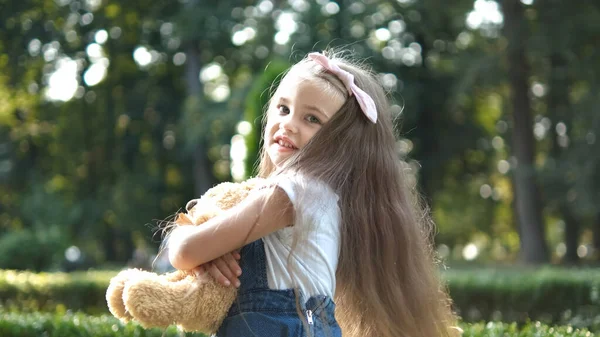 Menina pequena feliz brincando com seu brinquedo de ursinho de pelúcia favorito ao ar livre no parque de verão — Fotografia de Stock