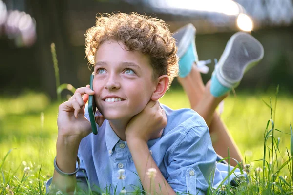 Šťastný dospívající chlapec mluví na mobilním telefonu venku v letním parku. Koncept přátelství online — Stock fotografie