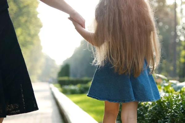 Mom and her small daughter with long hair walking together holding hands in summer park — Stock Photo, Image