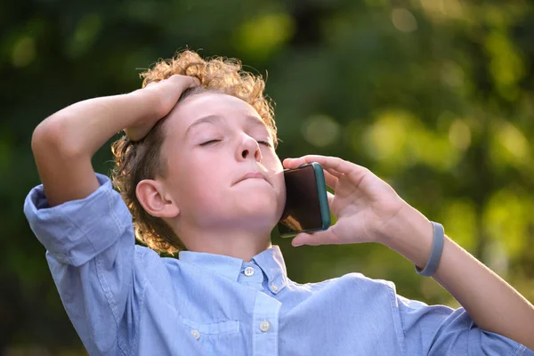 Chico joven discutiendo mientras habla por celular al aire libre en el parque de verano. Situaciones de conflicto en el concepto de la adolescencia — Foto de Stock