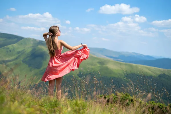 붉은 옷을 입고 여름철의 바람 이 부는 산에서 푸른 언덕 비탈에서 있는 행복 한 여자 여행자는 자연을 감상 한다 — 스톡 사진