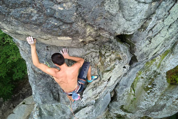 Young man climbing steep wall of rocky mountain. Male climber overcomes challenging route. Engaging in extreme sport concept — Stock Photo, Image