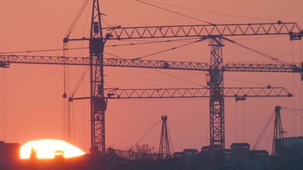 Dark silhouette of tower cranes with big setting sun at high residential apartment buildings construction site at sunset. Real estate development — Stock Video