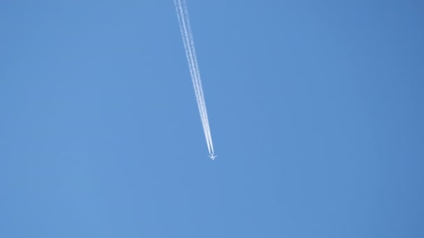 Távoli utasszállító repülőgép nagy magasságban repül a tiszta kék égen, fehér füstnyomokat hagyva maga után. Légiközlekedési koncepció — Stock videók