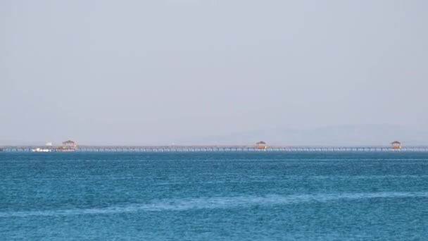 Seascape com superfície ondulada de água do mar azul com navio distante no final do longo cais flutuando em ondas calmas — Vídeo de Stock