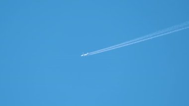 Mesafeli yolcu jet uçağı açık mavi gökyüzünde yüksek irtifada uçarken ardında beyaz duman izi bırakıyor. Hava taşımacılığı kavramı