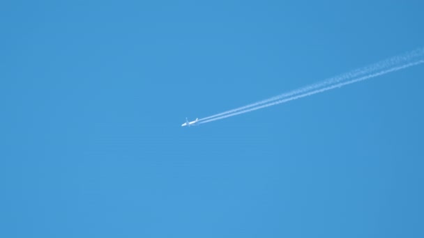 遠くの旅客機は、澄んだ青い空に高い高度を飛んで、白い煙の跡を後ろに残しています。航空交通の概念 — ストック動画