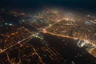 Uçak penceresinden gökyüzü manzarası ve şehrin yerleşim alanındaki aydınlık sokaklar. Yüksek irtifada karanlık şehir manzarası