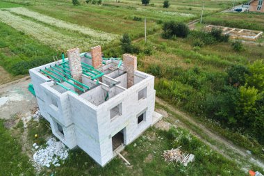 Havalandırılmış hafif beton duvarları ve inşaat halindeki ahşap çatı kirişleri olan bitmemiş özel evin havadan görüntüsü.