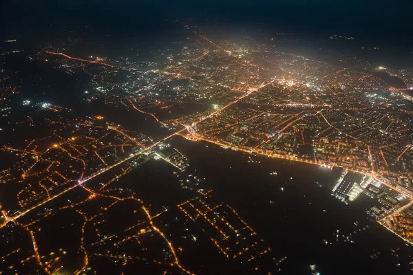 Widok z okna samolotu budynków i jasne oświetlone ulice w dzielnicy mieszkalnej miasta w nocy. Ciemny miejski krajobraz na dużej wysokości — Zdjęcie stockowe