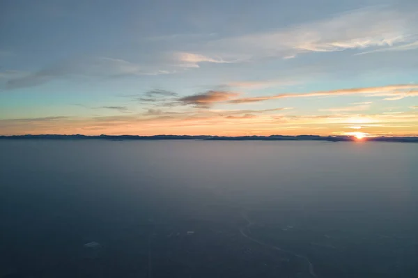 Widok z lotu ptaka kolorowy zachód słońca nad białą gęstą mgłą chmury pokrywają odległe ciemne sylwetki górskich wzgórz na horyzoncie — Zdjęcie stockowe