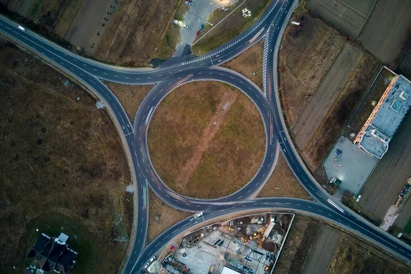 Aerial view of road roundabout intersection with fast moving heavy traffic at night. Top view of urban circular transportation crossroads. Rush hour with blurred car trail lights — Stock Photo, Image