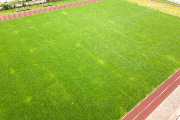 Futbol stadyumu sahasındaki yeşil çimlerin havadan görünüşü ve yazın kırmızı koşu yolları. — Stok fotoğraf