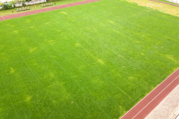 Vista aérea da superfície da grama verde recém-cortada no campo de estádio de futebol com pistas de corrida vermelhas no verão — Fotografia de Stock