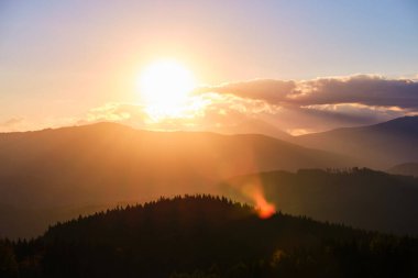 Güzel bir akşam panoramik manzarası. Gün batımında uzak dağ tepeleri üzerinde parlak batan güneş.
