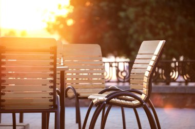 Şehir caddesinde gün batımında açık kafe sandalyeleri ve masa kapanıyor.