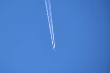 Mesafeli yolcu jet uçağı açık mavi gökyüzünde yüksek irtifada uçarken ardında beyaz duman izi bırakıyor. Hava taşımacılığı kavramı