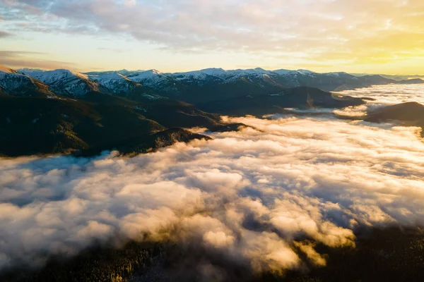 Вид с воздуха на яркий восход солнца над белыми плотными облаками с далекими темными горами на горизонте — стоковое фото
