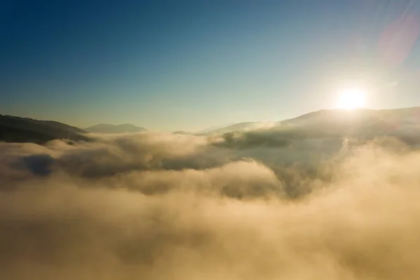 Vista aérea del vibrante amanecer sobre la densa niebla blanca con siluetas oscuras distantes de colinas de montaña en el horizonte —  Fotos de Stock