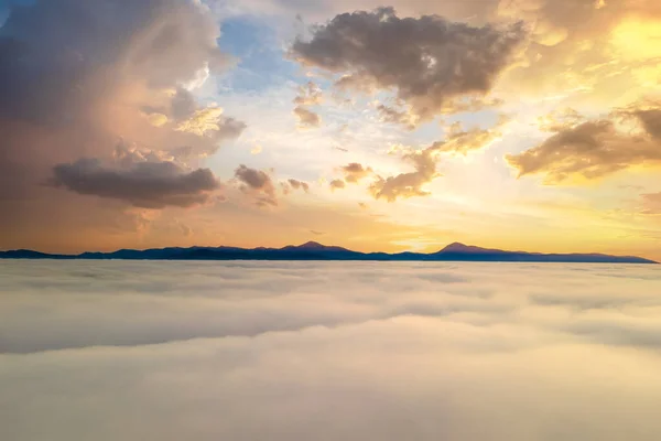 Vista aérea de la puesta de sol amarilla sobre nubes blancas hinchadas con montañas distantes en el horizonte —  Fotos de Stock