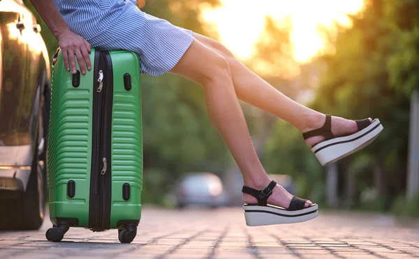 Primer plano de las piernas delgadas mujer joven descansando en la bolsa de la maleta al lado del coche. Concepto de viajes y vacaciones — Foto de Stock