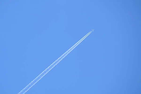 Μακρινό επιβατικό αεροπλάνο που πετά σε μεγάλο υψόμετρο στον καταγάλανο ουρανό αφήνοντας πίσω του ίχνη λευκού καπνού. Έννοια αεροπορικών μεταφορών — Φωτογραφία Αρχείου