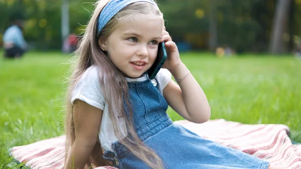 Glad barnflicka pratar på mobiltelefon i sommarparken — Stockfoto