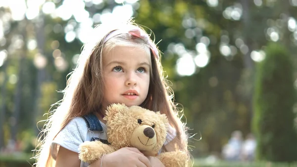 Glückliches kleines Mädchen spielt mit ihrem Lieblings-Teddybär-Spielzeug im Freien im Sommerpark — Stockfoto