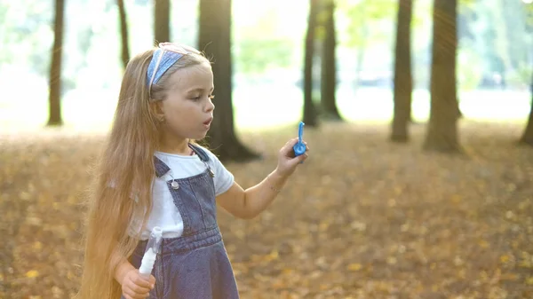 Joyeux petit enfant fille soufflant des bulles de savon à l'extérieur dans un parc vert. Activités d'été en plein air pour enfants concept — Photo
