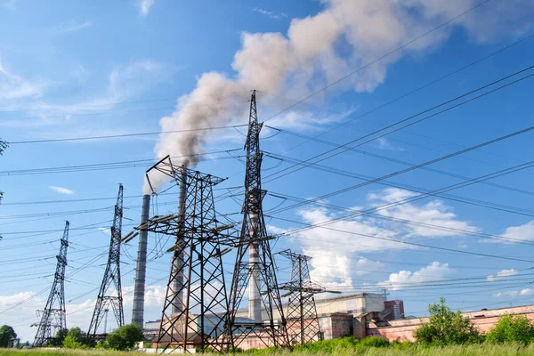 Pilones eléctricos de alto voltaje contra las tuberías altas de la central eléctrica de carbón con humo negro que se mueve hacia arriba contaminando la atmósfera. Producción de energía eléctrica con concepto de combustibles fósiles —  Fotos de Stock