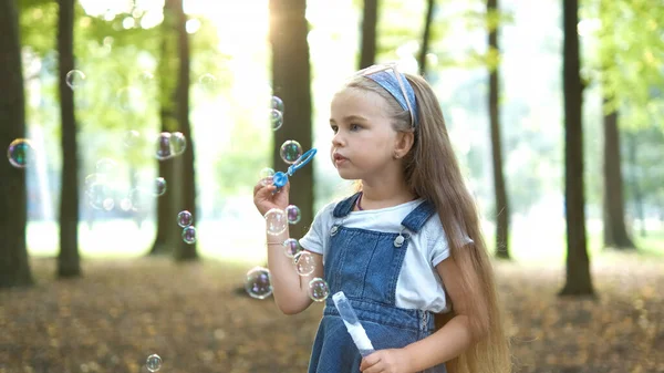 Pequeña niña feliz soplando burbujas de jabón al aire libre en el parque de verano —  Fotos de Stock